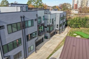Un edificio moderno de varios pisos con techo plano, ventanas grandes y un pequeño patio con césped verde y un carrito de golf.
