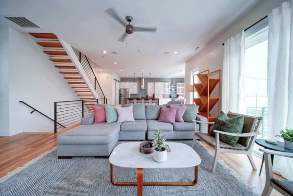 Una sala moderna con un sofá seccional gris, una mesa redonda de centro y una escalera con escalones de madera.