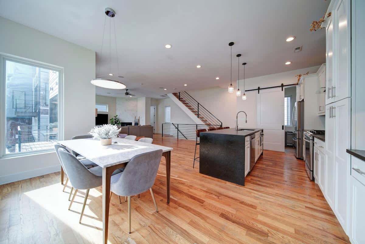 Una cocina moderna con piso de madera, un comedor con mesa y sillas, y una escalera que lleva a un nivel superior.