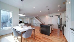 Una cocina moderna con piso de madera, un comedor con mesa y sillas, y una escalera que lleva a un nivel superior.