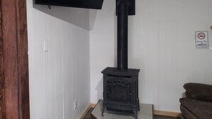 Una habitación con un estufa de leña negra, un televisor de pantalla plana montado y un cartel de prohibido fumar en la pared.