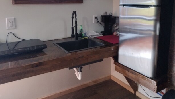 Una cocina con refrigerador de acero inoxidable, encimera negra, ventana sobre el fregadero y estante de madera.
