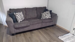 Un sofá gris con cojines estampados en una habitación con suelo de madera y pared blanca.