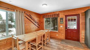 A wooden interior with a dining table and chairs, a red door, and large windows. - Big Timber - Cabin in McCall, ID (McCall)