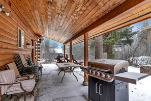 A covered patio with a wooden ceiling, a grill, and outdoor seating. - Big Timber - Cabin in McCall, ID (McCall)