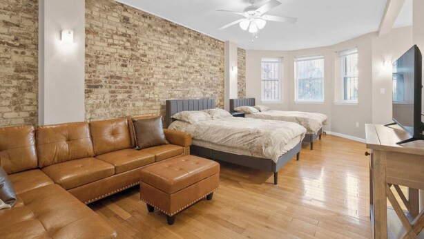 Ein modernes Schlafzimmer mit Backsteinwand, einem großen Bett, einer Couch und einem Fernseher.
