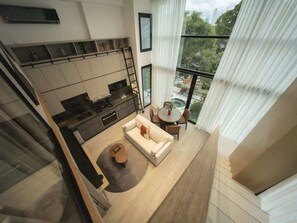 Ein modernes Wohnzimmer mit Sofa, Couchtisch und Esstisch. Im Hintergrund ist eine Küche erkennbar, und es gibt einen Balkon mit Blick ins Freie.