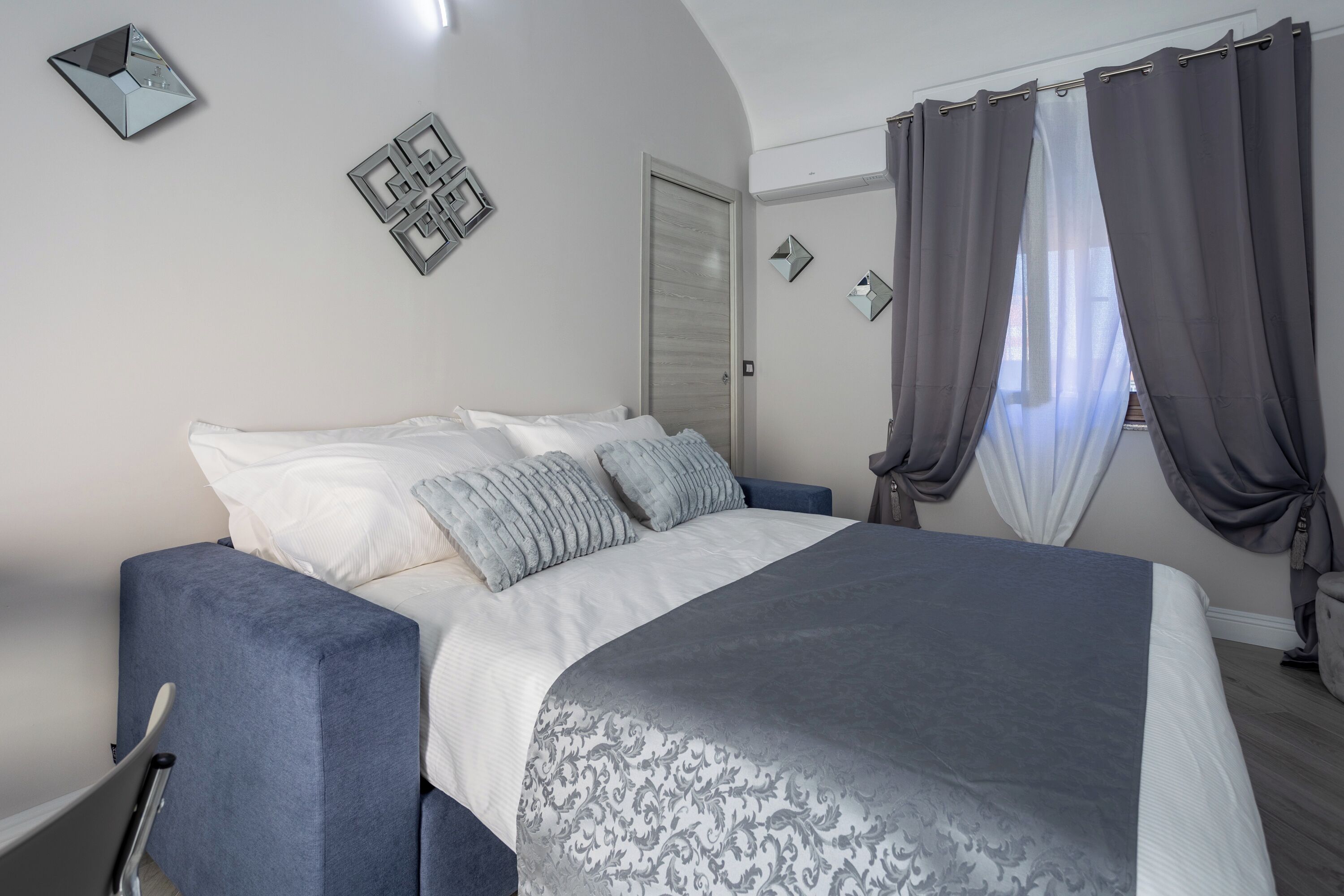 A bedroom with a bed, a chair, a wardrobe, and a window with curtains.