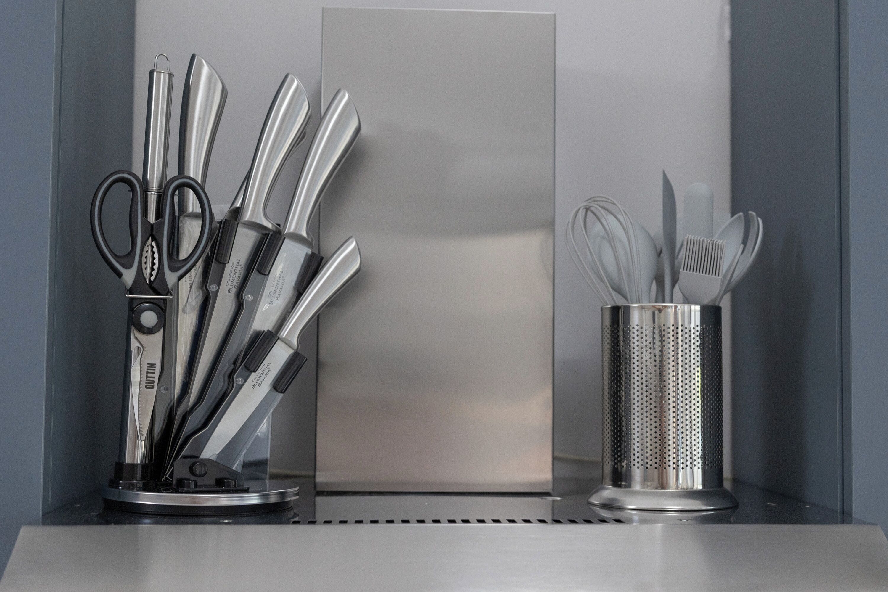 A kitchen counter with stainless steel utensils, including scissors, knives, and a grater, neatly arranged in a holder.