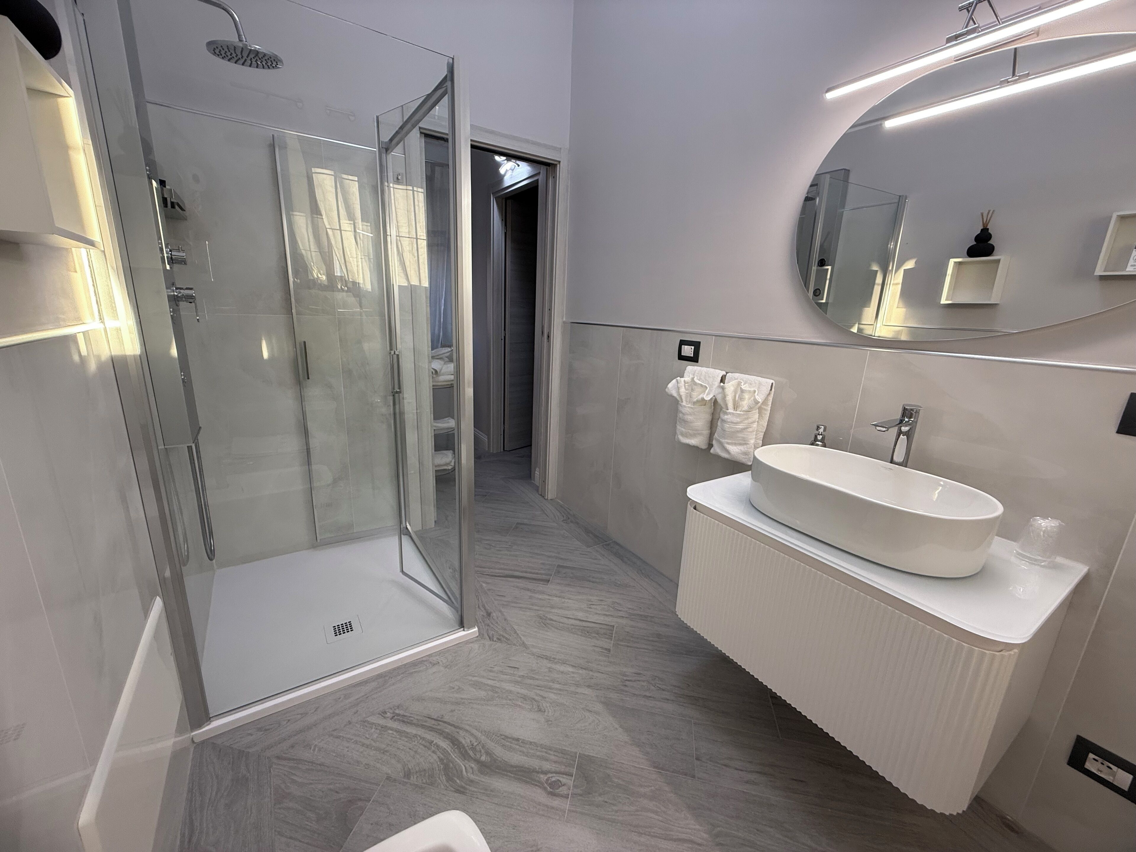 Une salle de bain moderne avec une douche à parois de verre, un lavabo blanc et un miroir doté d’un cadre rond.