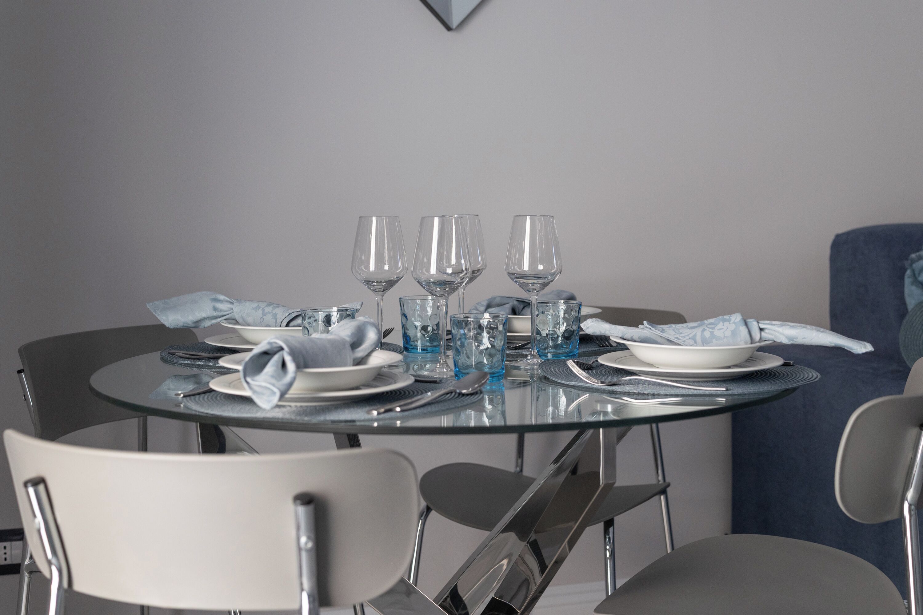 A round glass table set for four with plates, cutlery, and glasses.
