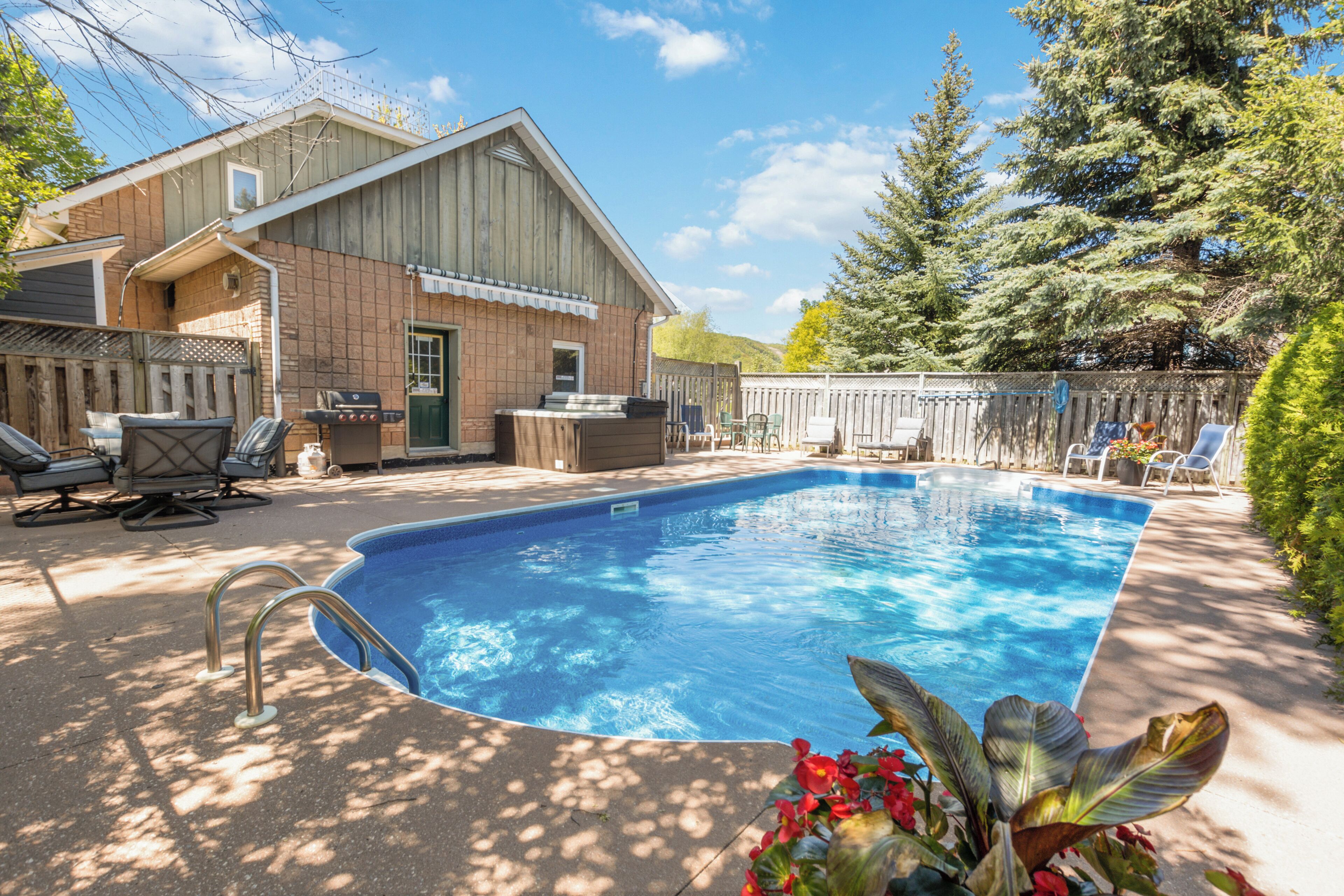 A rectangular swimming pool with a metal ladder, surrounded by a wooden deck and chairs.