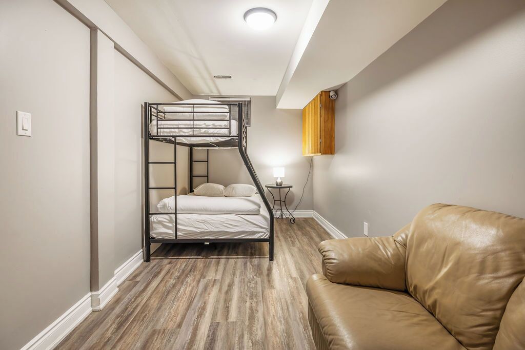 A bunk bed in a room with a wooden floor, a brown leather couch, and a small table with a lamp.