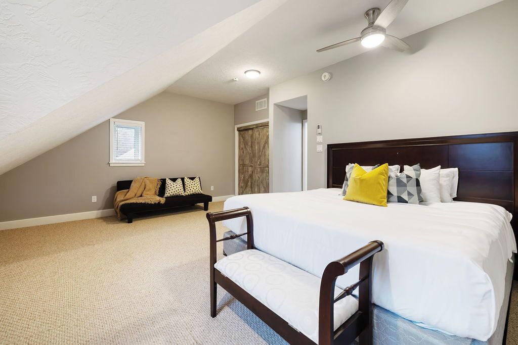 A bedroom with a large bed, a bench, a ceiling fan, and a window.