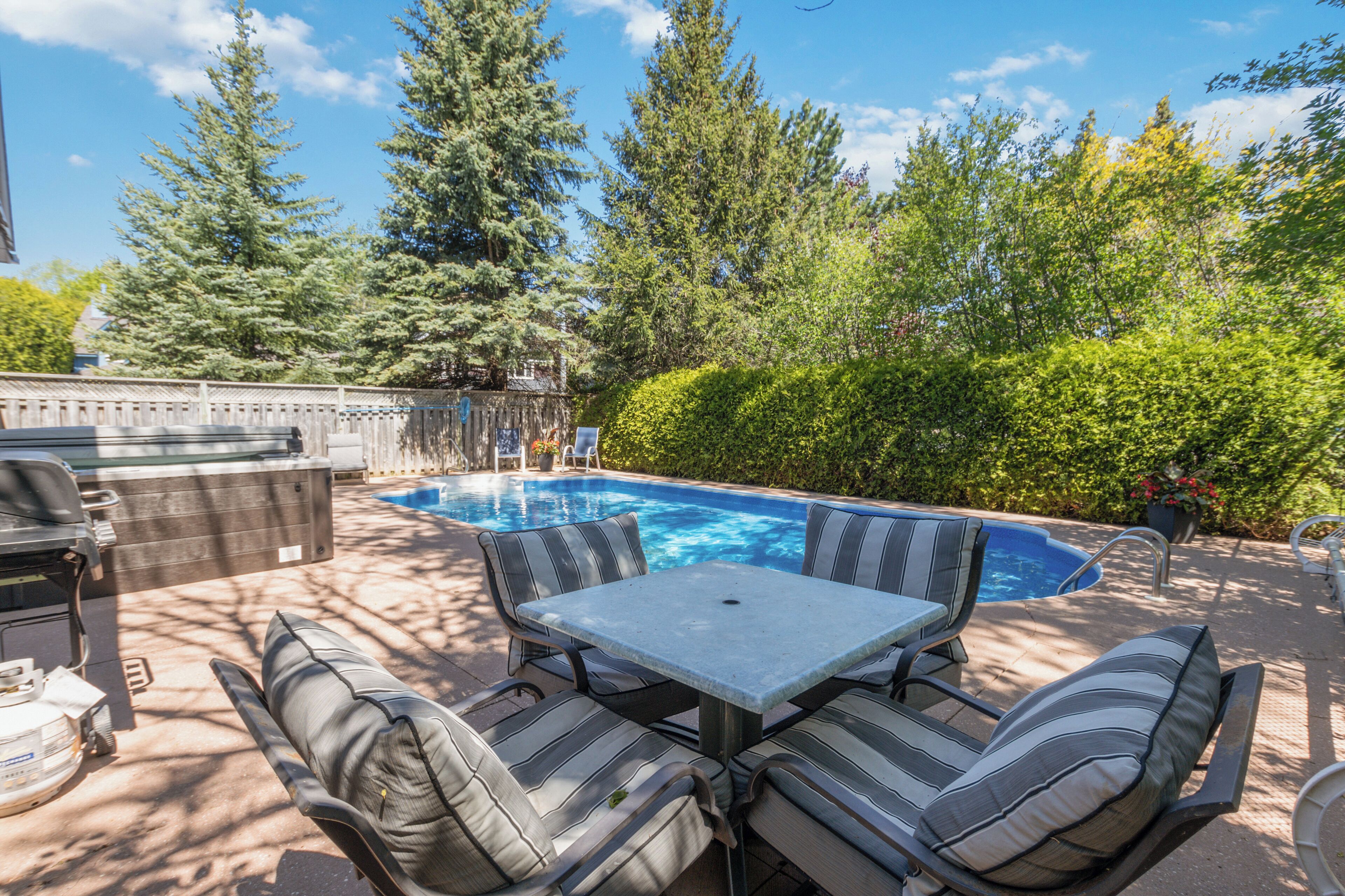 A backyard with a swimming pool, outdoor furniture, and a grill area.