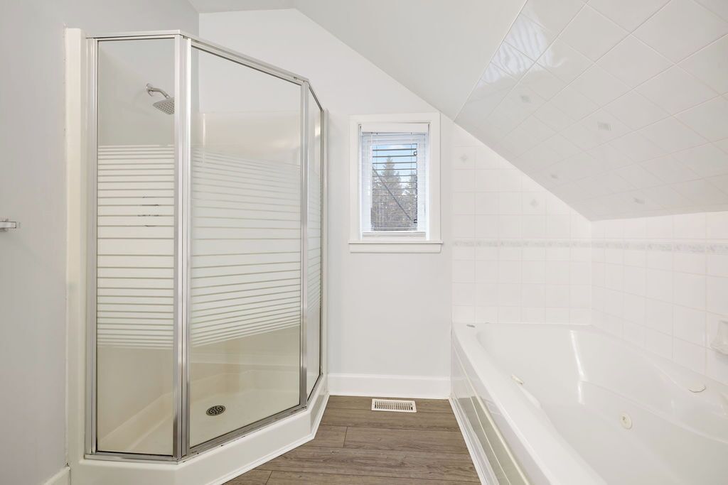 Un baño con cabina de ducha de vidrio, una ventana y una bañera.