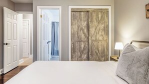 Een slaapkamer met een groot bed, een houten garderobe, een witte deur en een nachtkastje met een lamp.