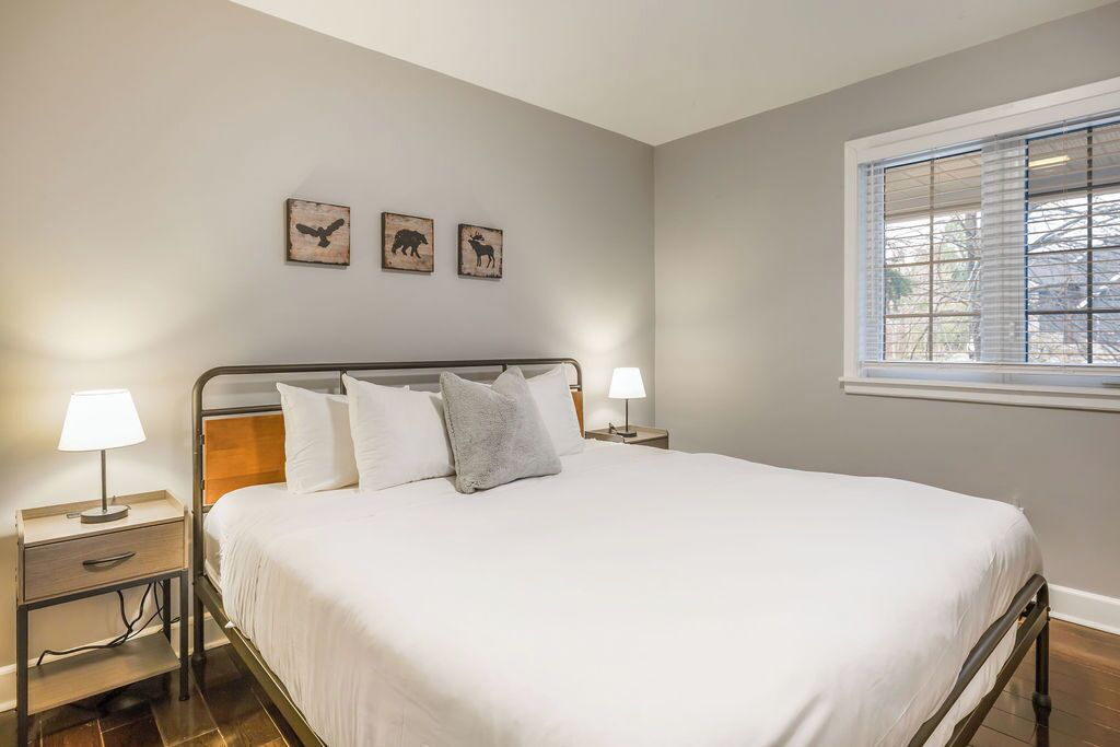 A neatly made bed with white linens and pillows, two bedside tables with lamps, and three wall-mounted animal-themed pictures.