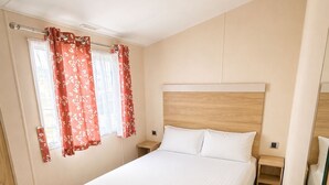 Habitación individual con una cama, cabecero de madera, una mesita de noche pequeña y un ventanal con cortinas rojas.