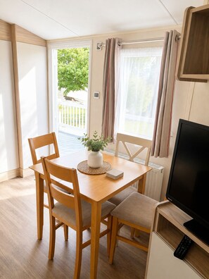 A compact living space with a dining table, two chairs, a television, and a window with curtains.