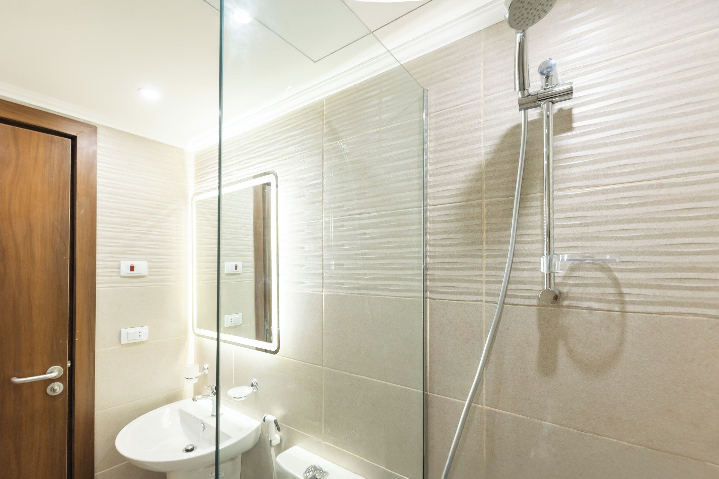 A bathroom with a glass shower enclosure, a sink, and a mirror.
