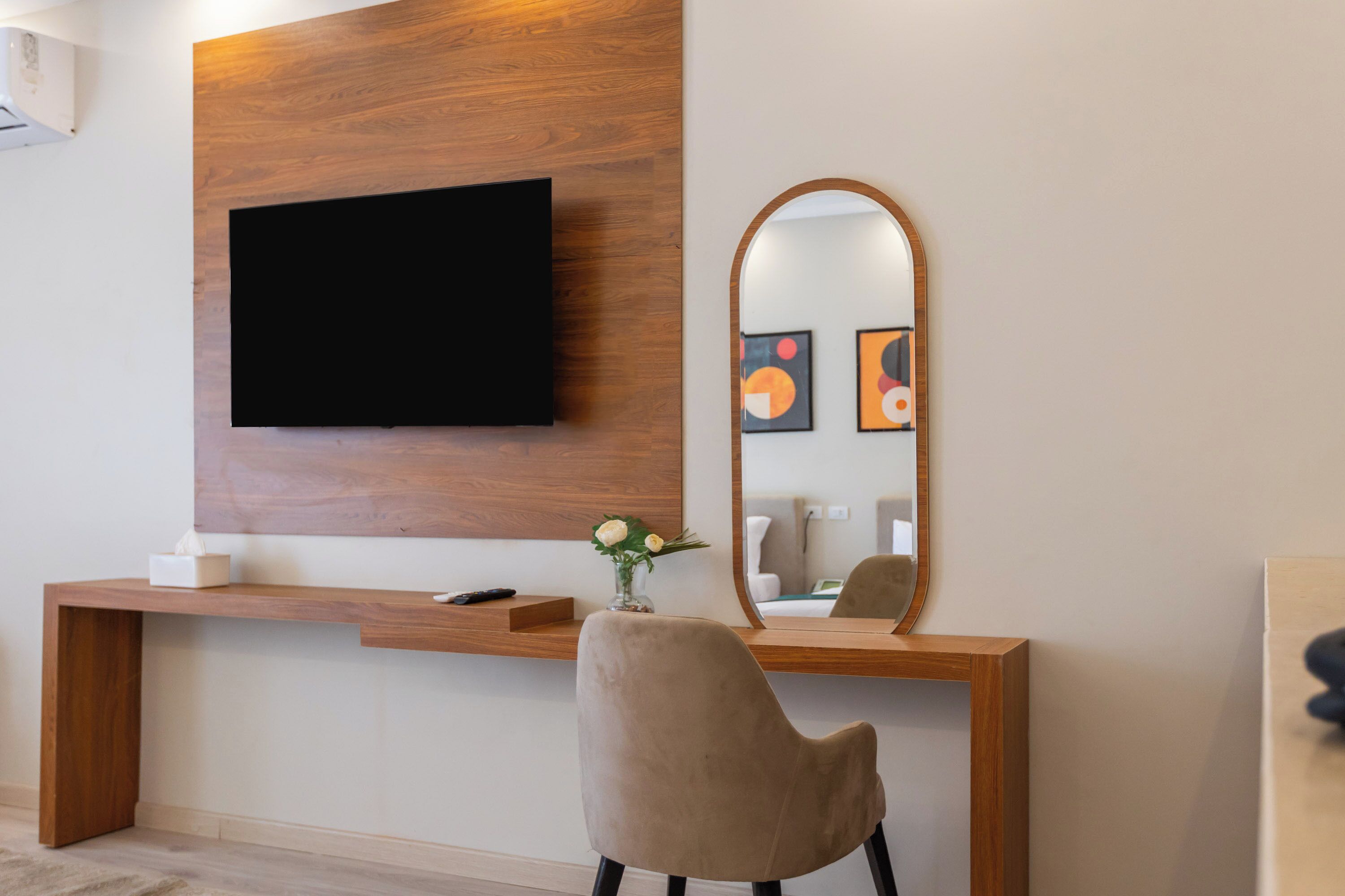 Una habitación moderna con una mesa consola de madera, un televisor montado, un espejo y una silla.