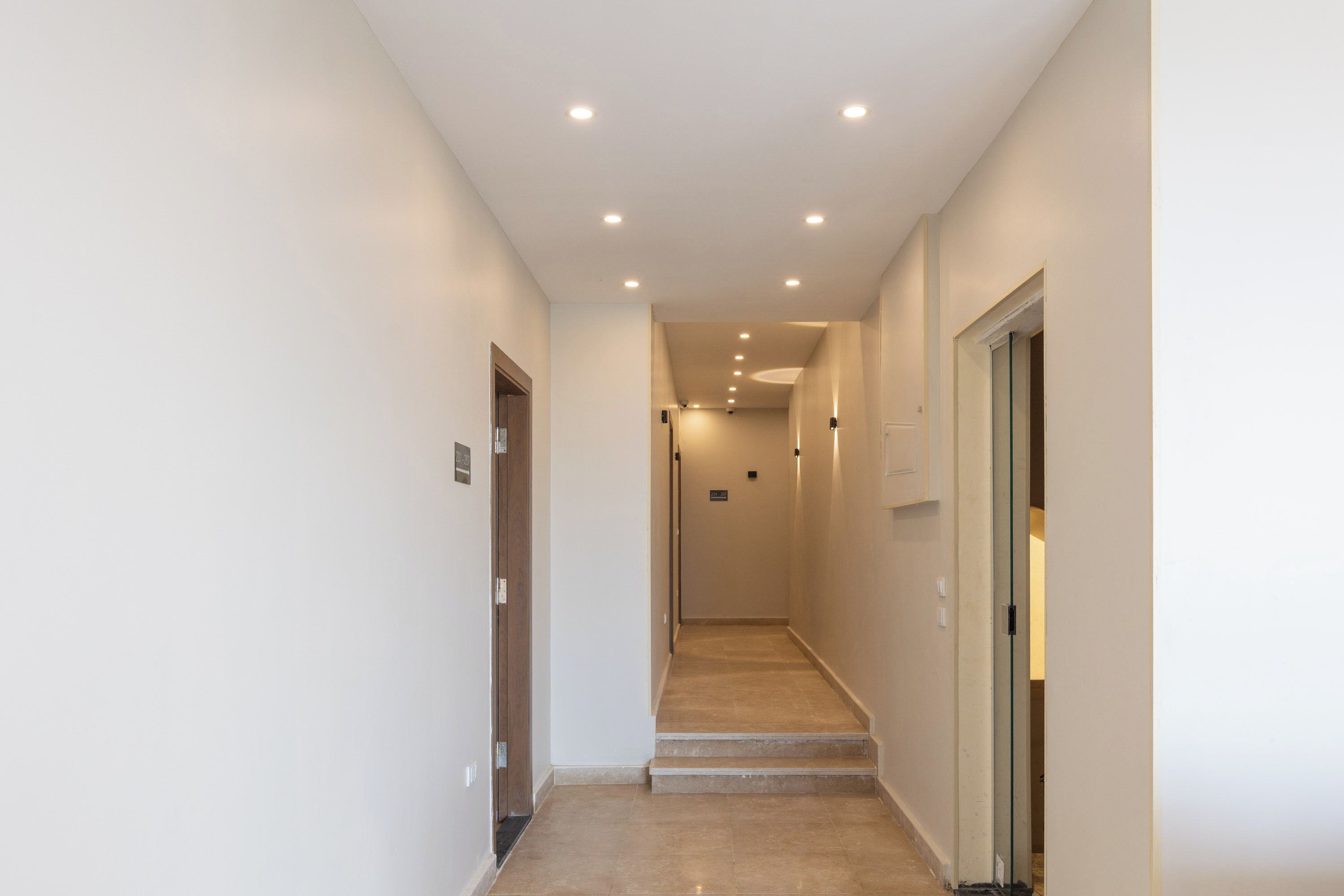 A narrow, well-lit hallway with a marble floor leading to a staircase.