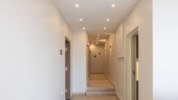 A narrow, well-lit hallway with a marble floor leading to a staircase.