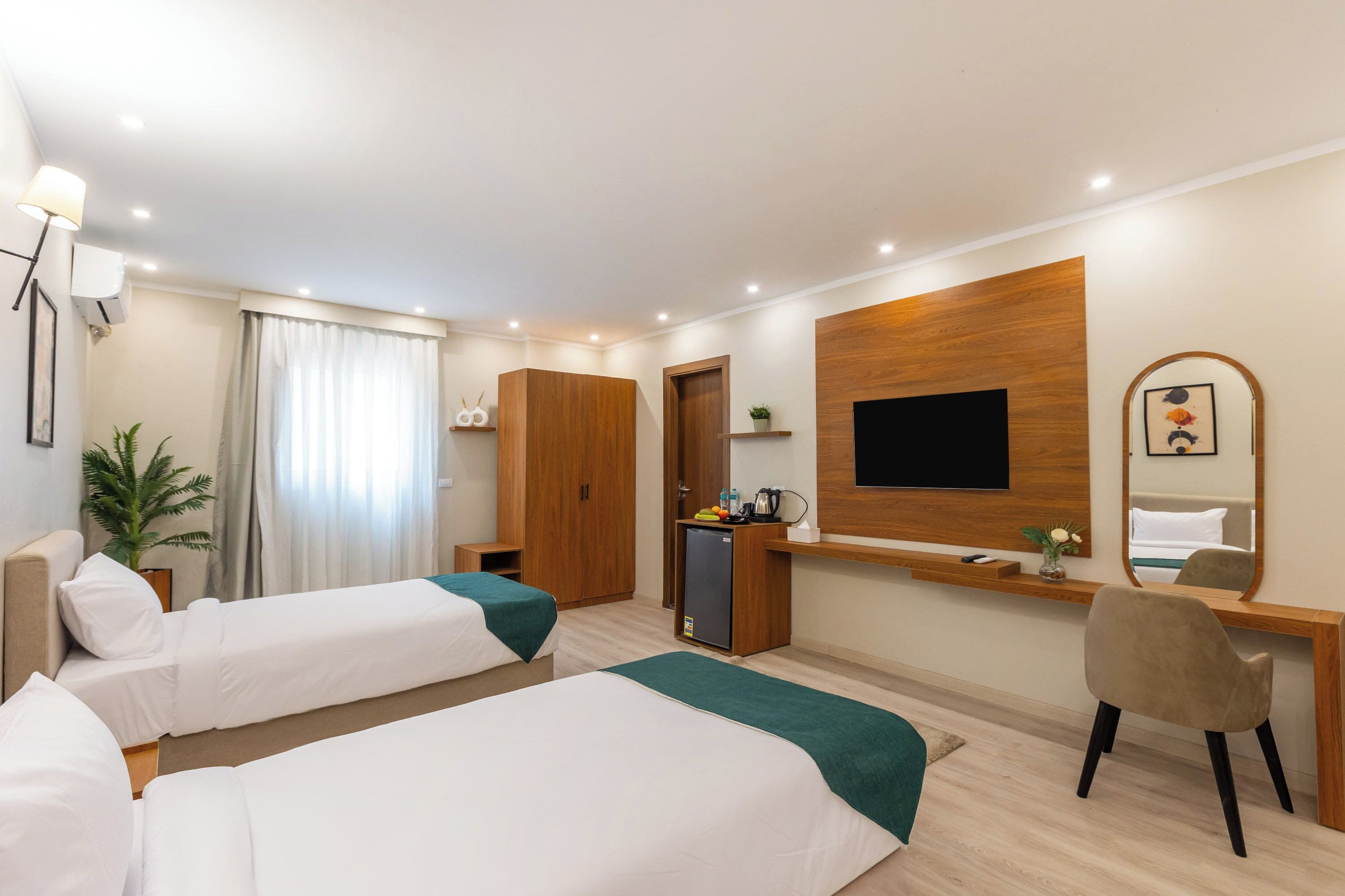 Quarto de hotel com duas camas, uma escrivaninha, uma cadeira, uma televisão e uma pequena cozinha.
