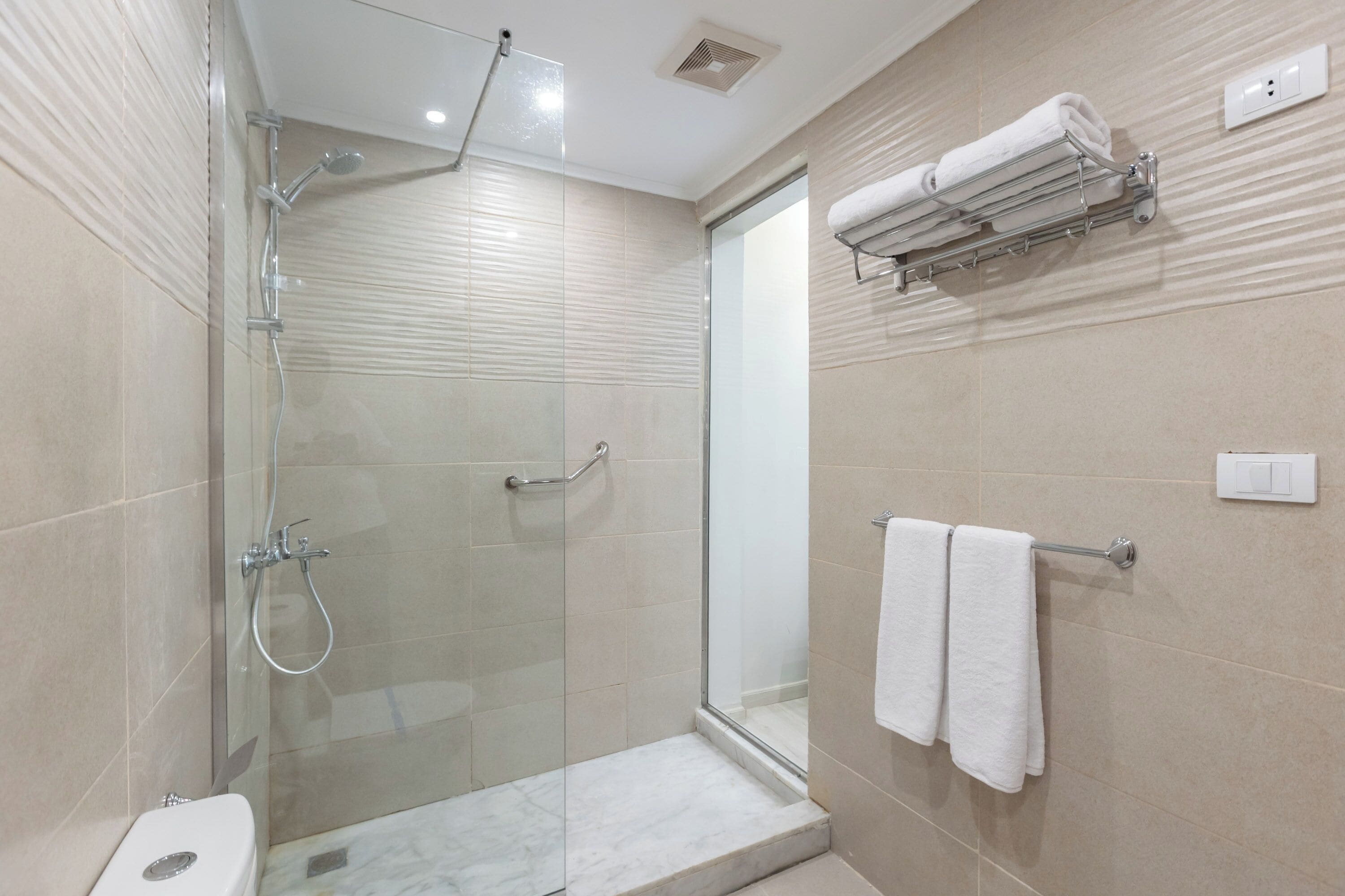 A modern bathroom with a glass-enclosed shower, a toilet, and a towel rack with two towels.