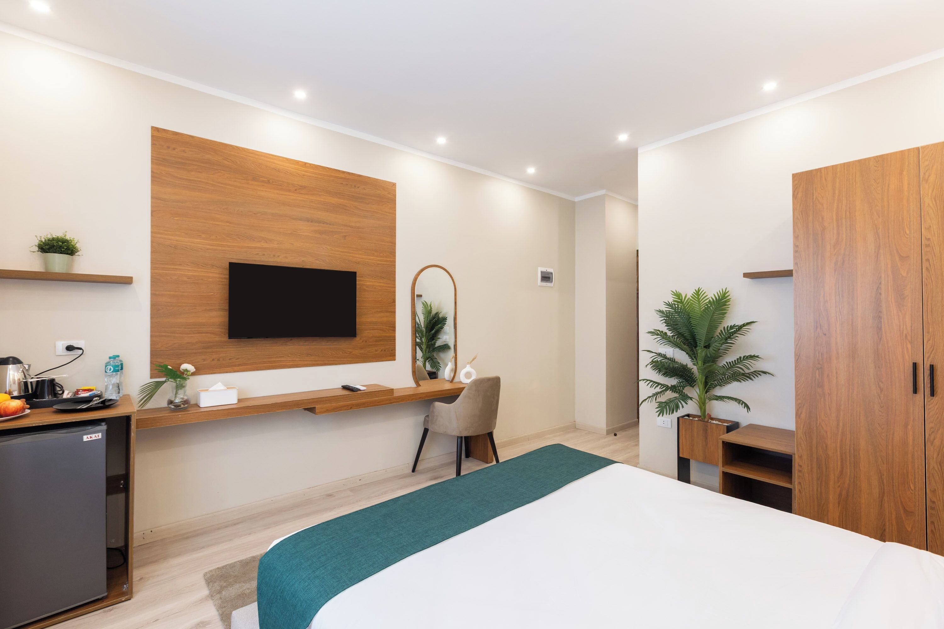 Una habitación de hotel moderna con una cama, un escritorio, un televisor montado en la pared, un armario y una pequeña kitchenette.