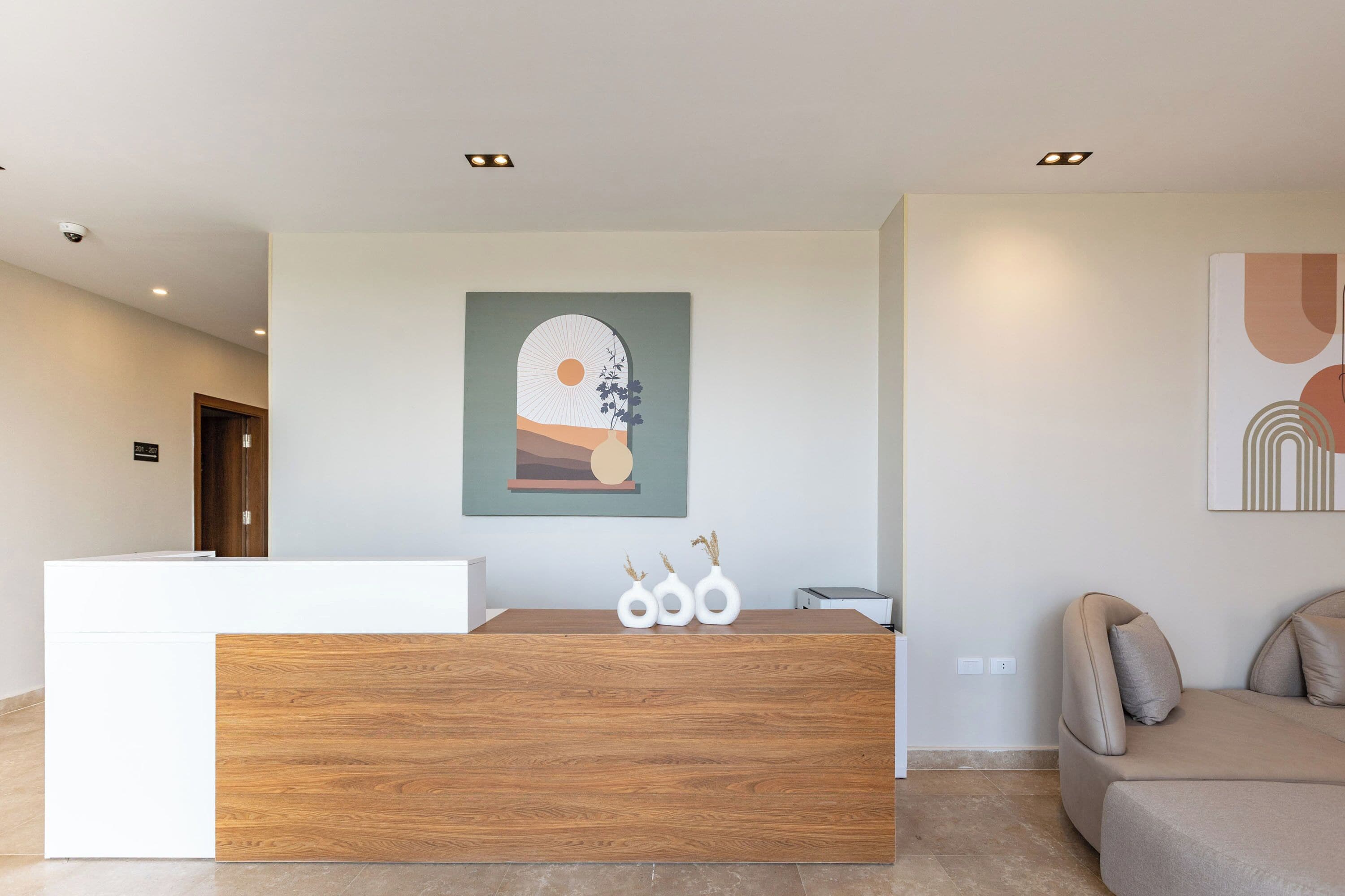 Una reception con piano in legno e base bianca, affiancata da un divano beige e un'opera d'arte appesa al muro.