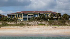 A beachfront property with a two-story building, a sandy beach in the foreground, and a clear sky. - Beachfront Paradise! Dog friendly 3 bedroom condo! (Flagler Beach)