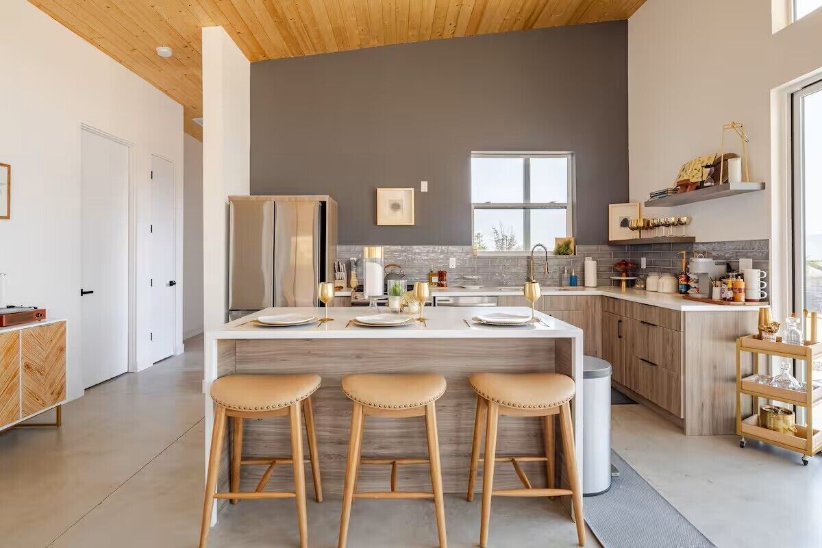 Een moderne keuken met een centraal eiland, barkrukken, een koelkast en een raam voor natuurlijk licht.