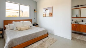 Ein Schlafzimmer mit einem großen Bett, einem Fenster, einem Gemälde und einem Badezimmer mit Waschbecken und Schränken.