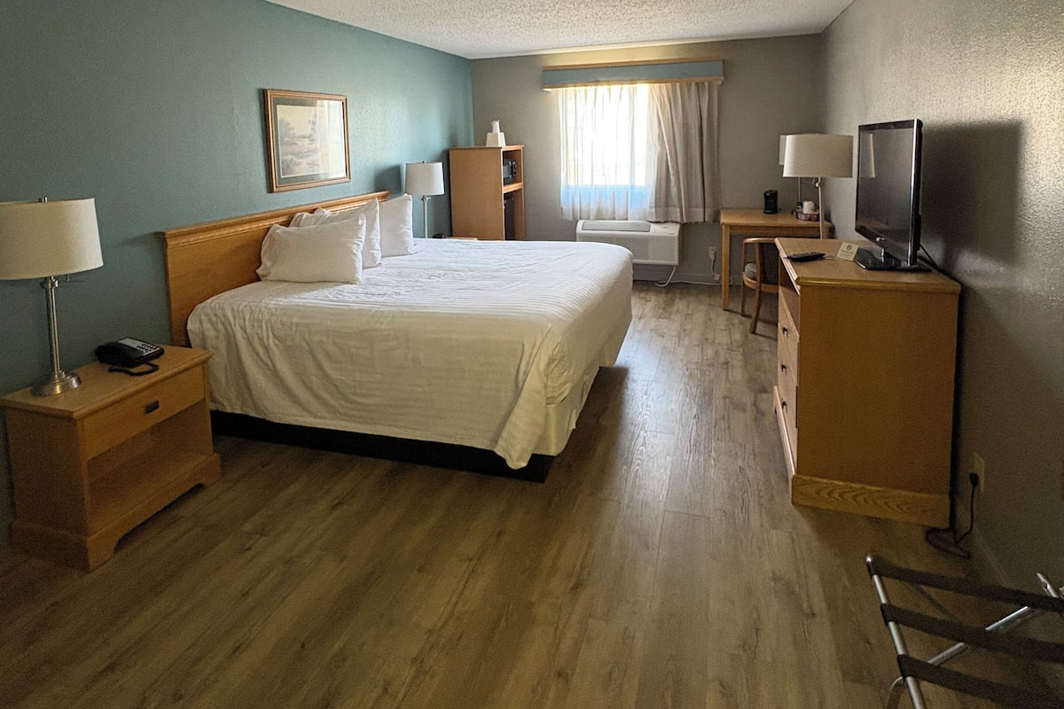 A hotel room with a bed, bedside tables, a desk, a television, and a window with curtains.