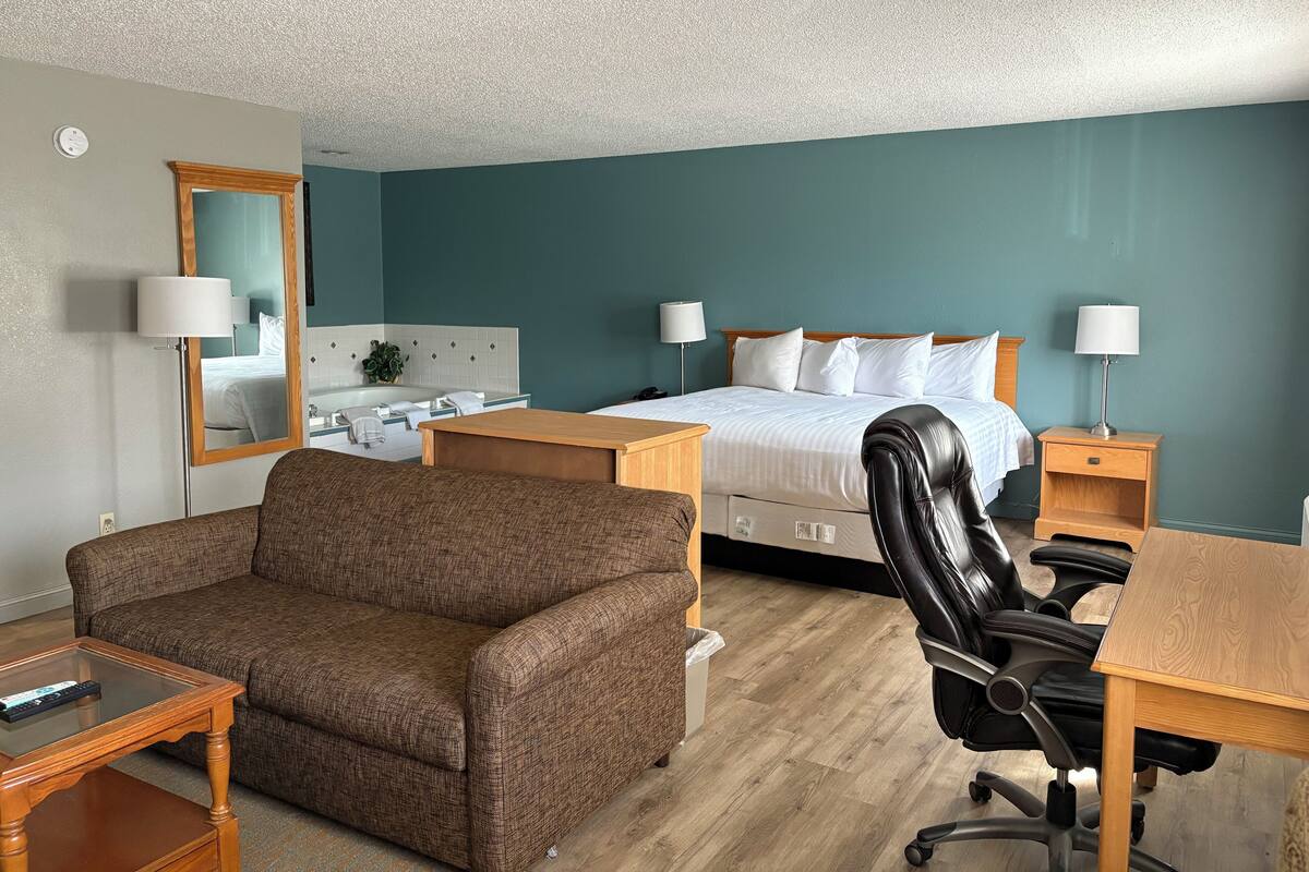 A hotel room with a bed, a desk, a chair, a sofa, and a bathroom with a bathtub.
