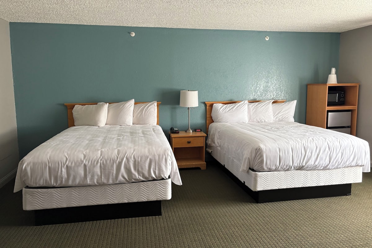 A hotel room with two beds, a nightstand with a lamp, a microwave, and a small cabinet.