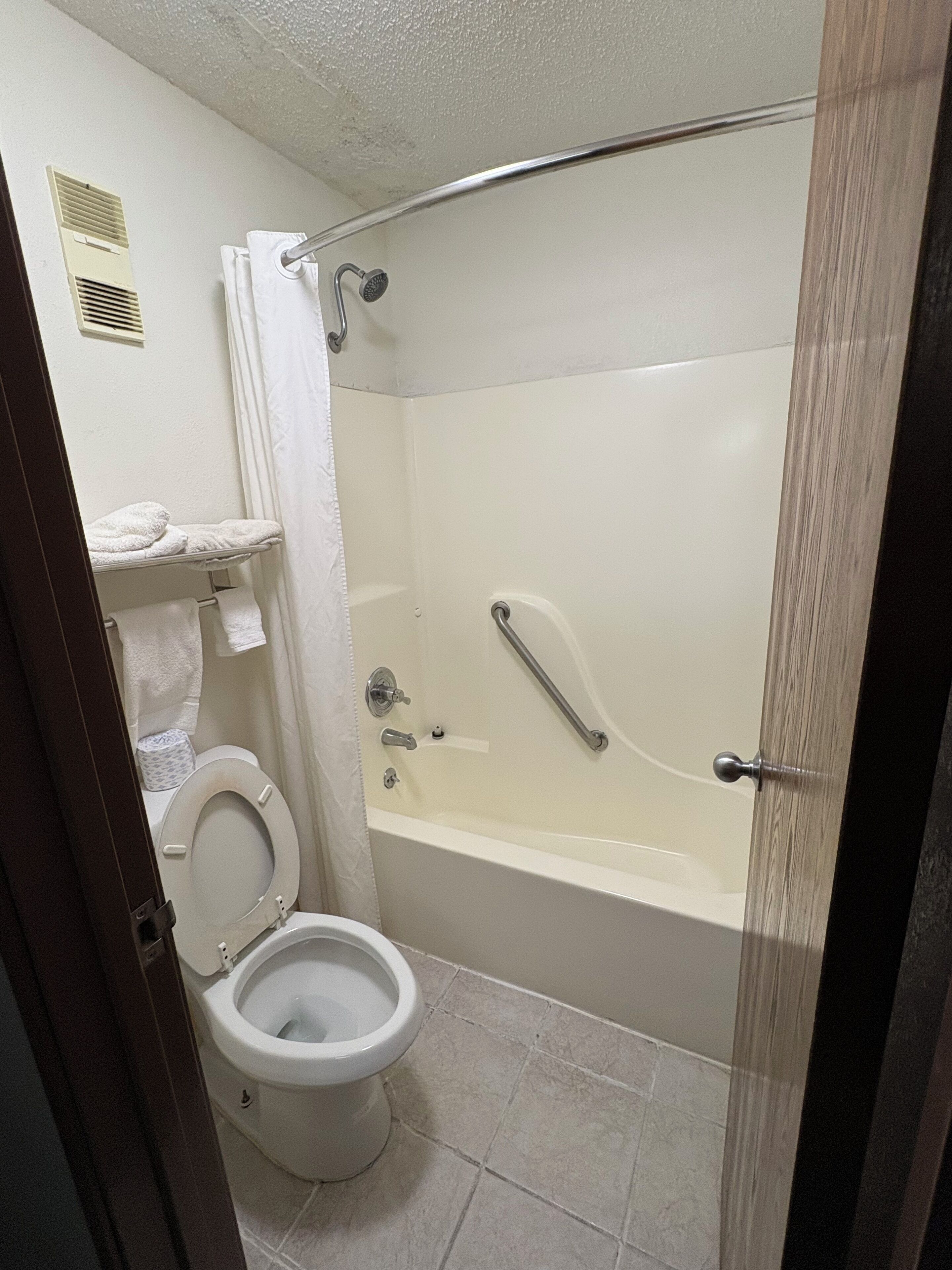 Une salle de bain équipée de toilettes, d’une baignoire, d’un rideau de douche et d’un porte-serviettes.