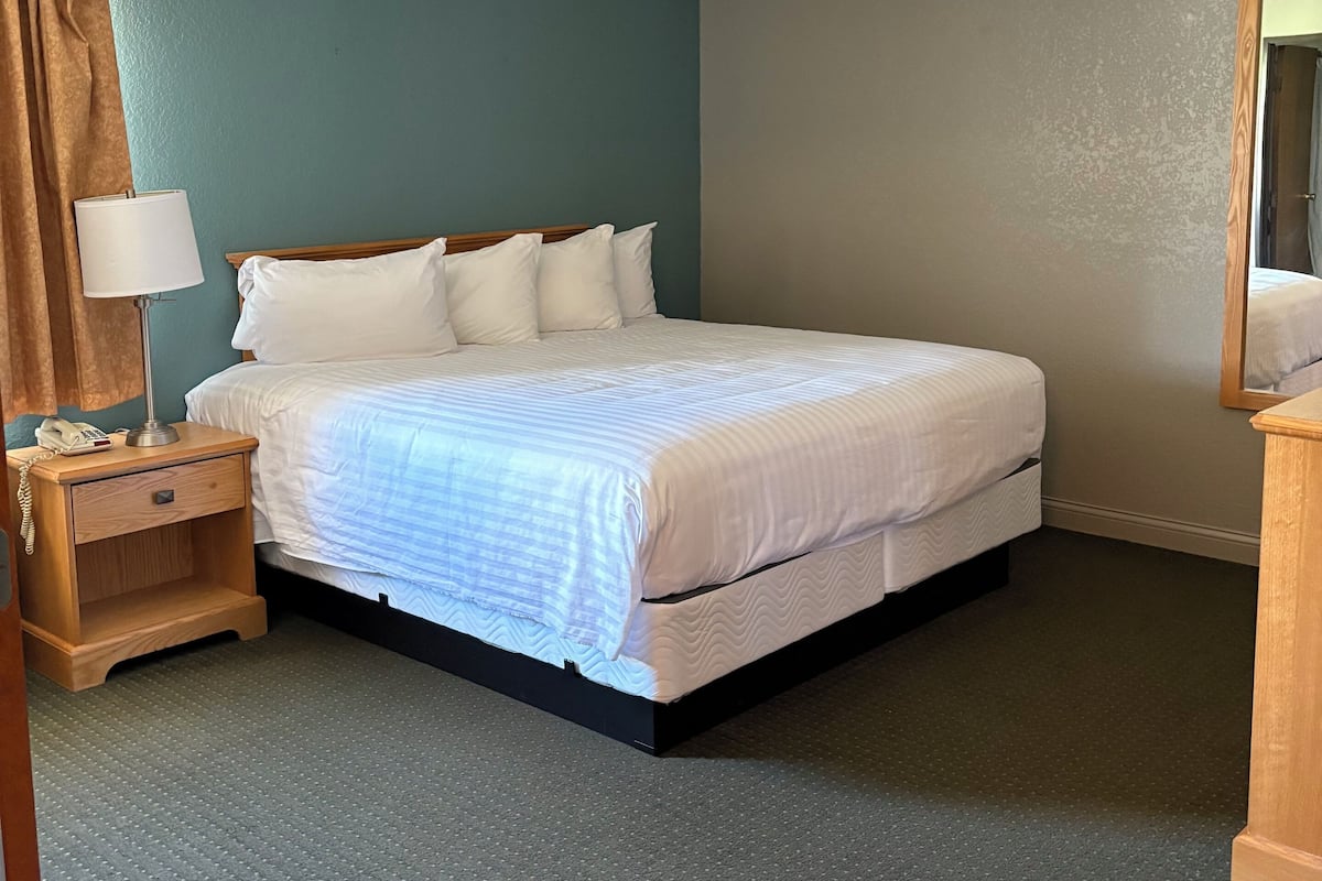 A neatly made bed in a room with teal walls, a wooden nightstand with a lamp, and a mirror.