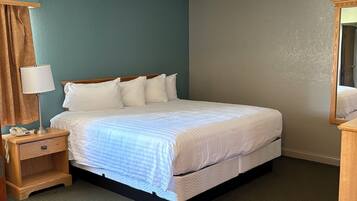 Een opgemaakt bed in een kamer met turquoise wanden, een houten nachtkastje met een lamp en een spiegel.