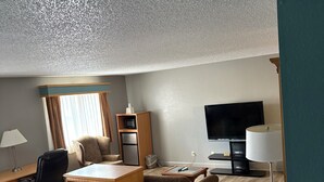 A hotel room with a wooden desk, a chair, a sofa, a TV, and a lamp. - Simply Home Inn & Suites (Robinson)