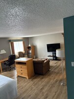 Habitación de hotel con un escritorio de madera, una silla, un sofá, un televisor y una lámpara.