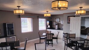 A dining area with tables and chairs, a kitchen in the background, and a door leading to another room. - Simply Home Inn & Suites (Robinson)