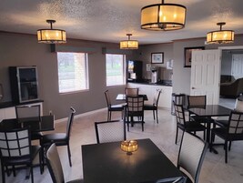 Un comedor con mesas y sillas, una cocina al fondo y una puerta que da a otra habitación.