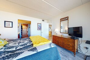 Ein Hotelzimmer mit einem Bett, einem Schminktisch, einem Fernseher und einer Tür zu einem anderen Raum.