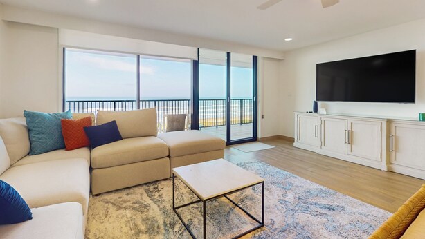 Una sala moderna con un sofá beige, una mesa de centro, un televisor de pantalla plana y un balcón con vistas.