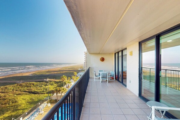 A balcony with a view of the beach, a table and chairs, and a small rug. - Sweeping View, Luxe Perks: Suntide III - Unit 708 (South Padre Island)