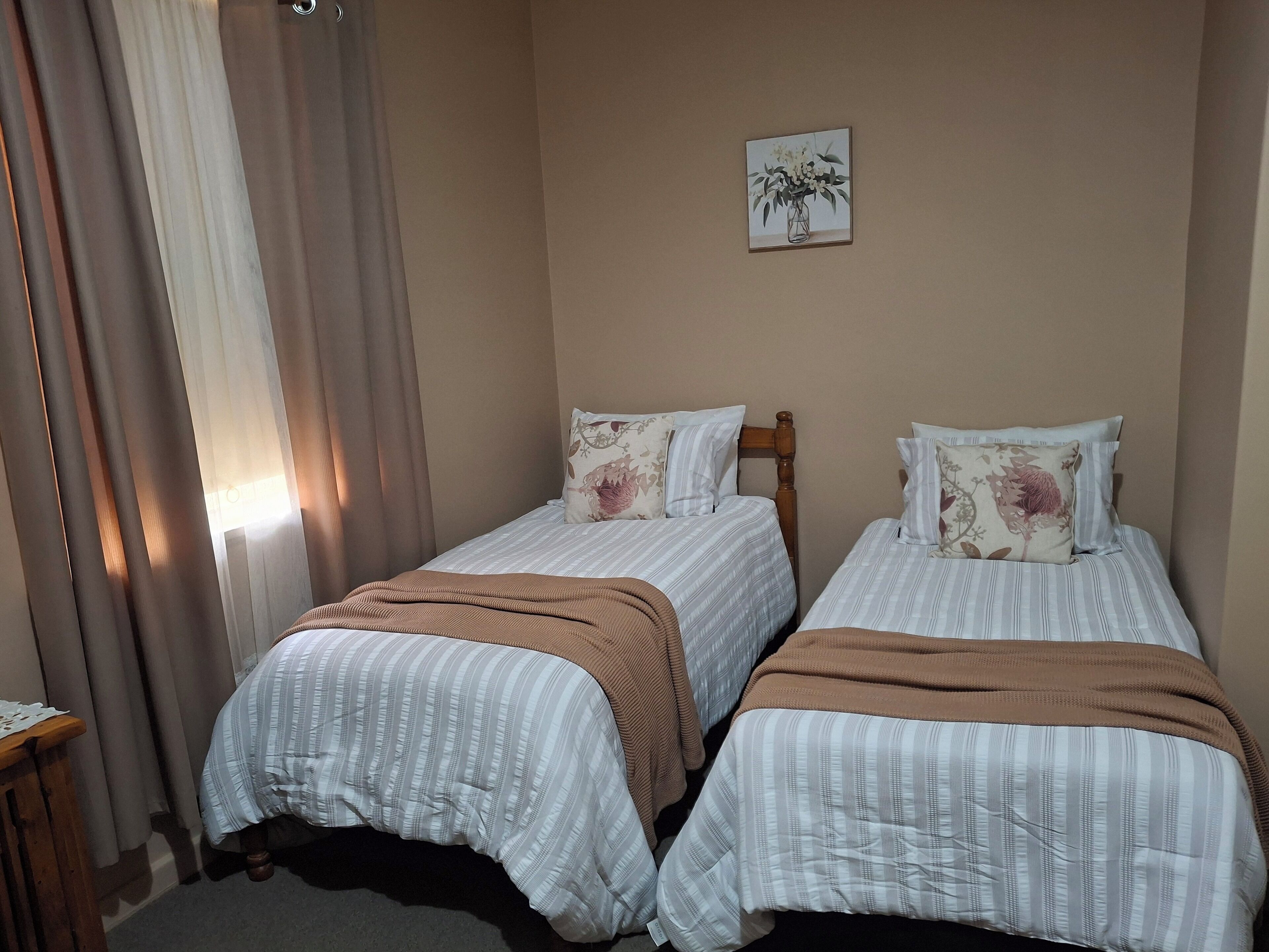 A room with two beds, each with striped bedding and floral pillows, a wooden headboard, and a framed picture on the wall.