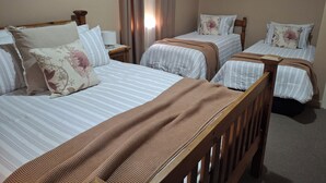 Une chambre d’hôtel avec deux lits simples, chacun doté d’une tête de lit en bois, de draps à rayures blanches et d’oreillers à motifs floraux. Il y a deux tables de chevet avec des lampes, et les murs de la chambre sont de couleur beige et ornés d’œuvres d’art florales.